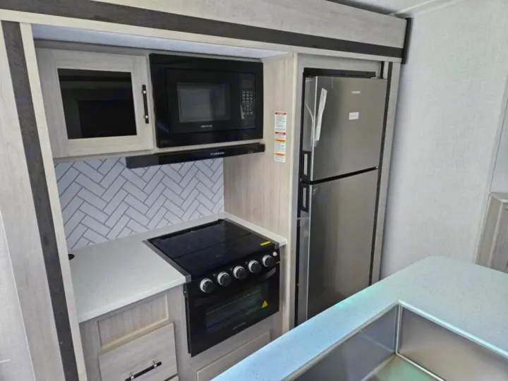 Modern RV rental kitchen features stainless steel fridge, microwave, stove, and a sleek sink on speckled counters.. Crossroads RV Sunset Trail Super Lite 2025
