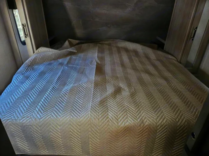 Cozy RV rental bedroom features a neatly made bed with a beige chevron quilt, framed by light wood cabinets.. Crossroads RV Sunset Trail Super Lite 2025