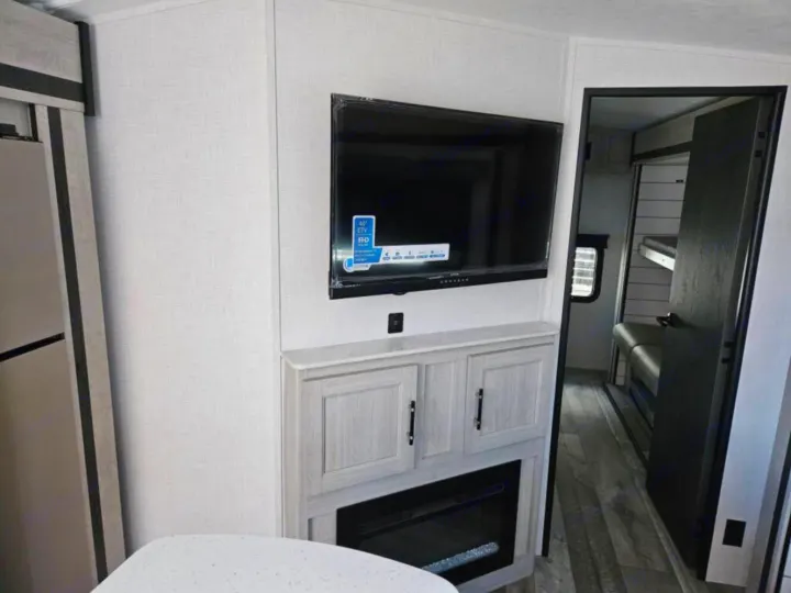 Modern RV rental interior: living area with TV, electric fireplace, and doorway to bunks. Enjoy cozy travel amenities.. Crossroads RV Sunset Trail Super Lite 2025