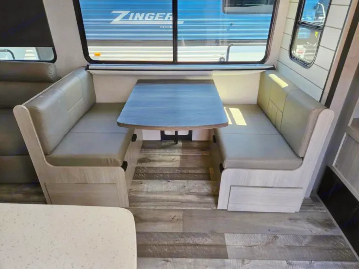 Cozy RV rental dinette: two cushioned benches, wood-grain table. Bright interior with a window view.. Crossroads RV Sunset Trail Super Lite 2025