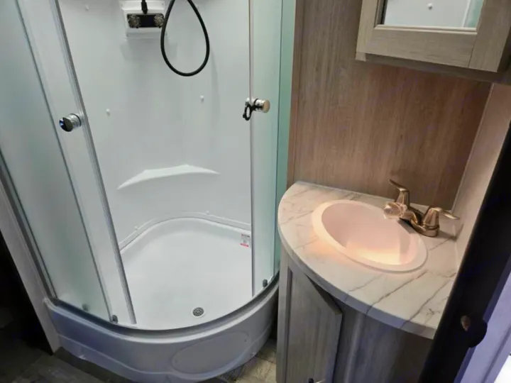 Explore this compact RV rental bathroom, featuring a corner shower with glass doors and a functional vanity sink.. Crossroads RV Sunset Trail Super Lite 2025