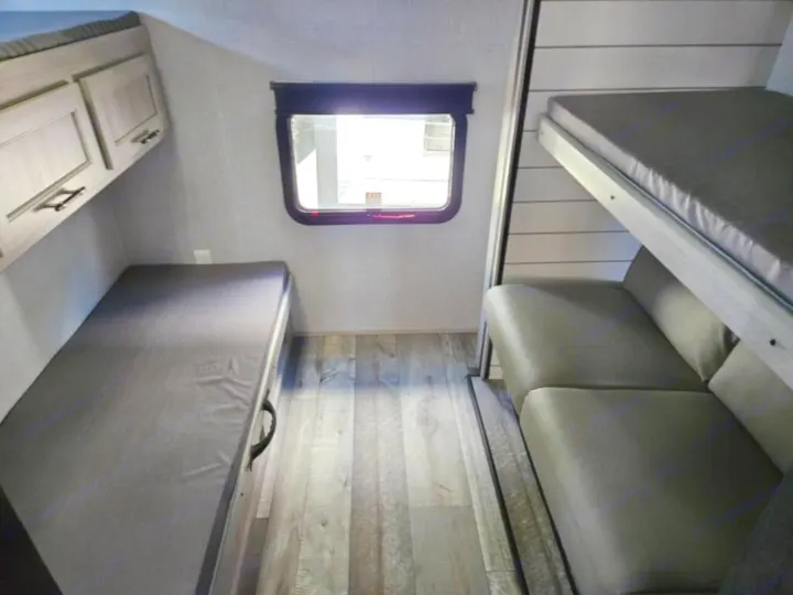 Cozy rv rental interior featuring a bunk bed on the left, stacked bunks, a sofa on the right, and a window for comfortable camper stays.. Crossroads RV Sunset Trail Super Lite 2025