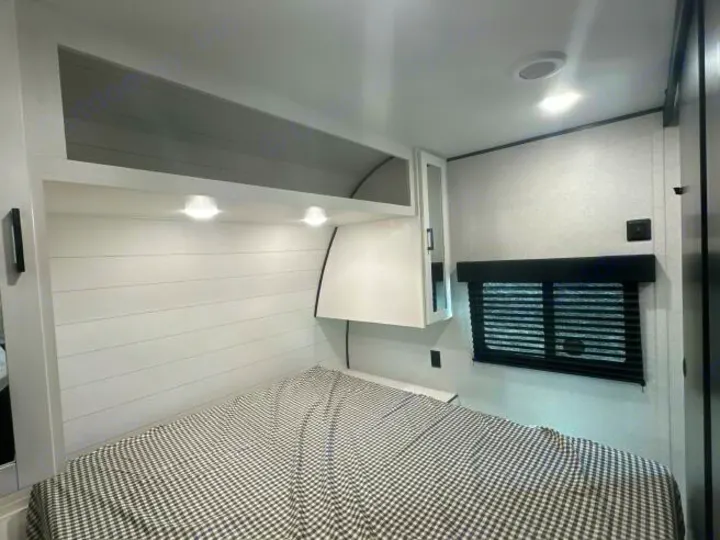 Modern RV rental bedroom interior features a checkered bed, shiplap headboard, overhead storage, and window.. Jayco Jay Flight 2026