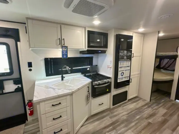 This RV rental kitchen features white cabinets, stone-look counters, stove, microwave, fridge, sink, and bunk beds visible.. Jayco Jay Flight 2026