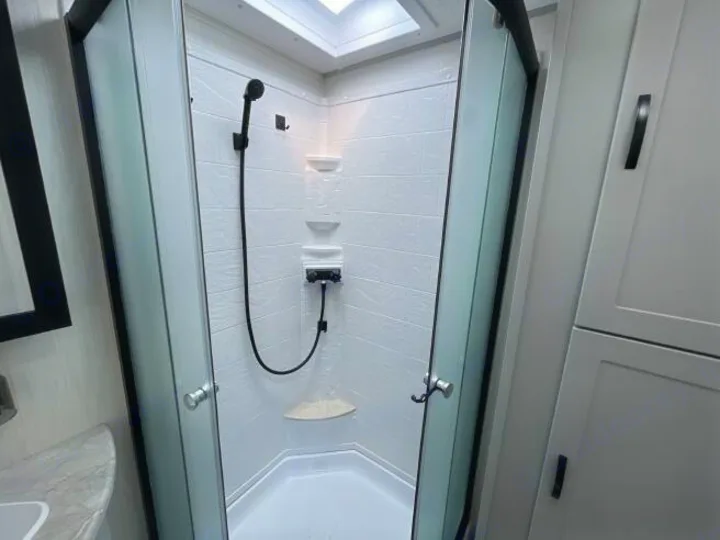 Spotless RV rental shower with clear glass doors, black fixtures, and a bright skylight. Modern, compact bathroom amenity.. Forest River Vibe 2023