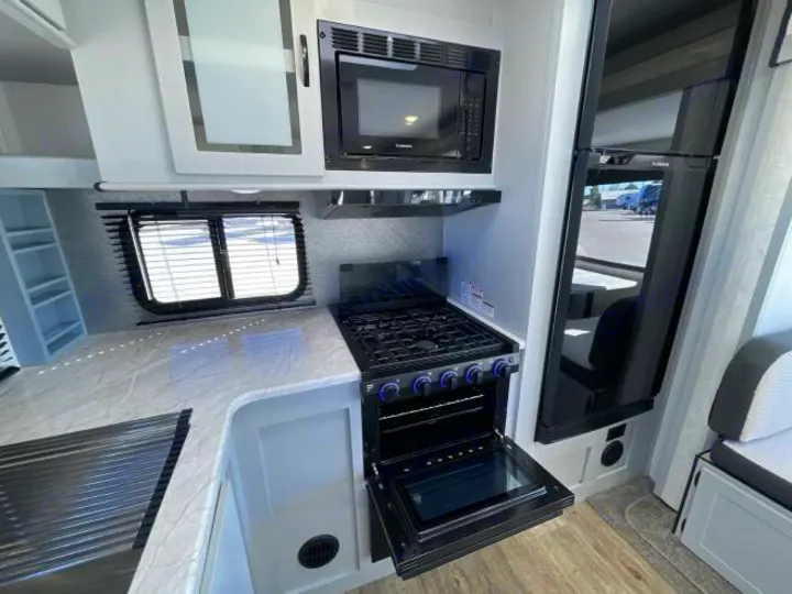 Modern RV rental galley featuring microwave, stove/oven, and large fridge. Cook comfortably on your road trip adventure.. Forest River Vibe 2023