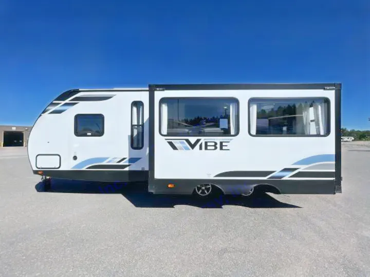 White Vibe travel trailer, a spacious RV rental with slide-out extended, parked on asphalt under a clear blue sky.. Forest River Vibe 2023