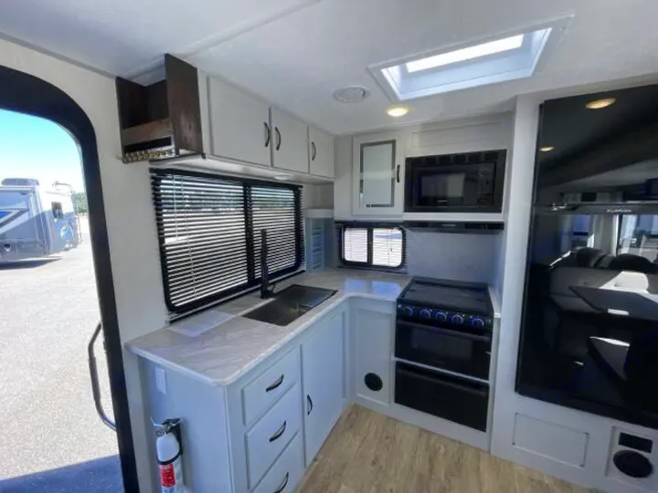 Inside an RV rental: a modern kitchen with light cabinets, a black sink, stove, microwave, and large fridge, plus a skylight.. Forest River Vibe 2023