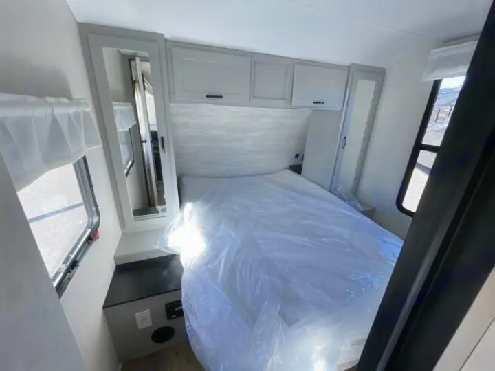 This modern RV rental bedroom offers a clean bed, overhead cabinets, and compact storage. Ready for your next trip!. Forest River Vibe 2023