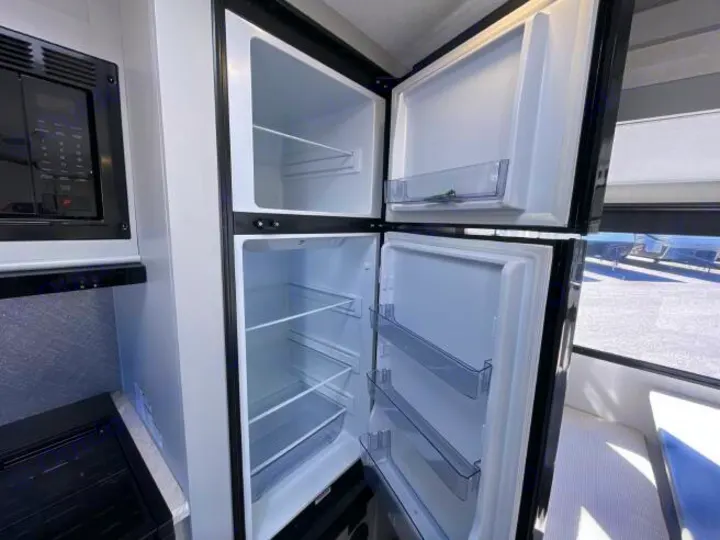 Clean, empty RV rental kitchen with an open refrigerator, freezer, and microwave oven, ready for your travels.. Forest River Vibe 2023