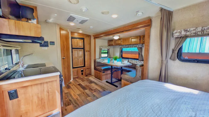 RV rental interior featuring a compact kitchen, cozy dinette with seating, and a glimpse of the bed, all with warm wood finishes.. Forest River Rockwood Mini Lite 2018