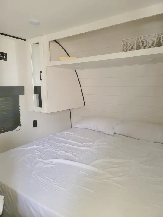 Cozy, modern white bedroom in an RV rental, featuring a comfortable bed, overhead storage, and mirrored cabinet.. Jayco 260BH 2026