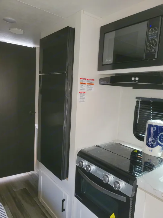 Modern RV rental kitchen with a black refrigerator, Invision microwave, and stove with oven. White cabinets and sleek interior.. Jayco 260BH 2026