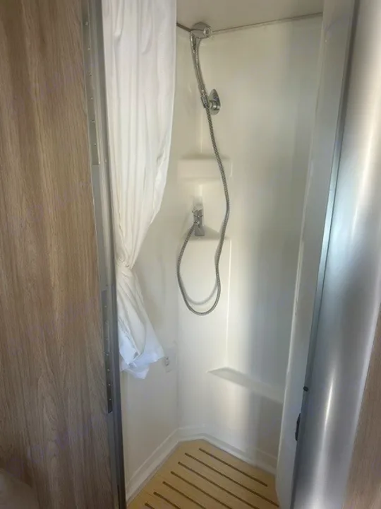 Compact shower in an RV rental, featuring a handheld showerhead, white interior, and wooden slatted floor mat.. Winnebago EKKO 2026