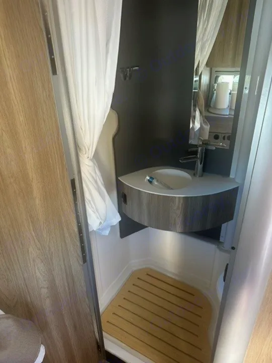 Explore this efficient rv rental bathroom: shower with wooden mat, corner sink, and mirror for compact comfort.. Winnebago EKKO 2026