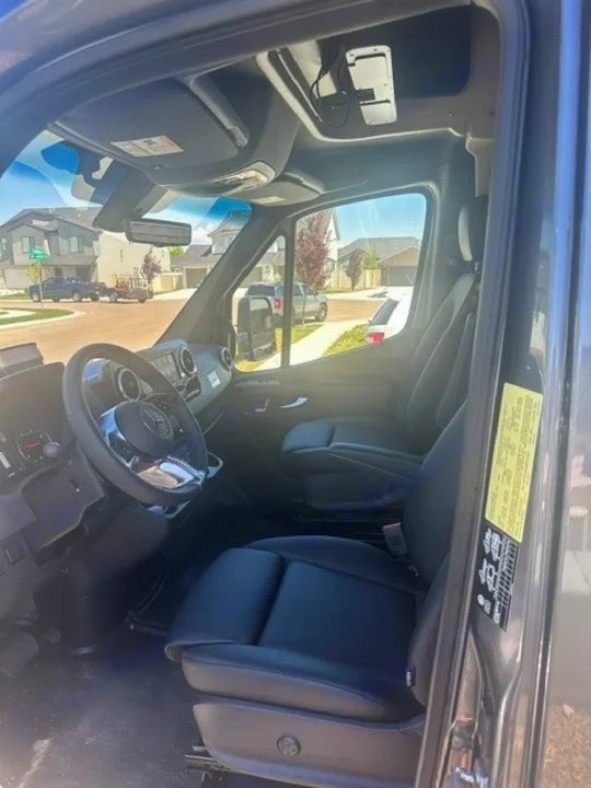Spacious interior of a modern rv rental van. Features black leather driver & passenger seats, steering wheel, and dashboard.. Winnebago EKKO 2026