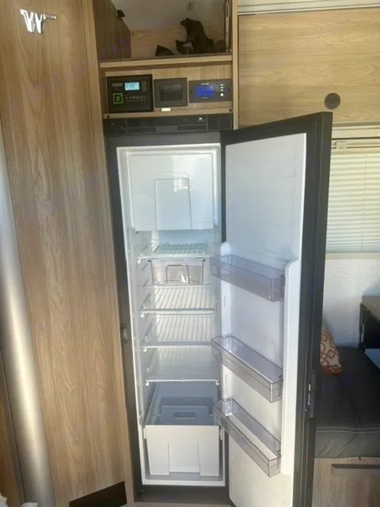 Empty refrigerator and freezer unit in a clean RV rental, with system control panels visible above, ready for your trip.. Winnebago EKKO 2026