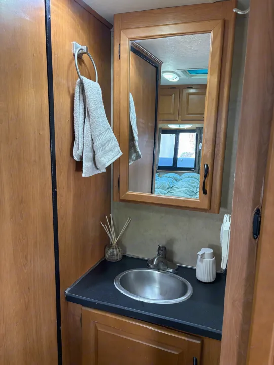 RV rental bathroom vanity with sink, mirror (reflecting bedroom), towel, and soap dispenser. Compact and functional design.. Thor Majestic 2013
