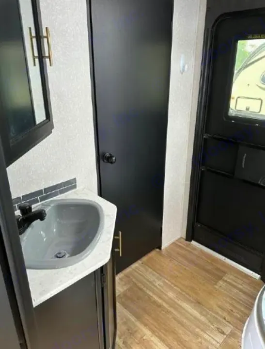RV rental interior showing a compact bathroom vanity with a gray sink, black faucet, dark cabinet, and wood-look floor.. Forest River Cherokee Grey Wolf 2022