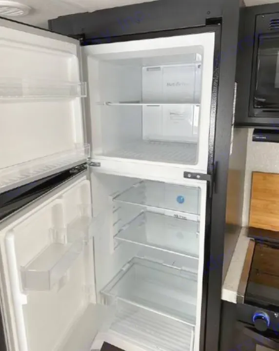 Empty RV rental refrigerator & freezer with open doors, showing its clean interior, shelves, and bins.. Forest River Cherokee Grey Wolf 2022