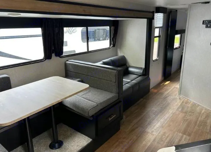 Modern rv rental living space: dinette with storage, black faux-leather sofa, and light wood flooring for comfortable travel.. Forest River Cherokee Grey Wolf 2022