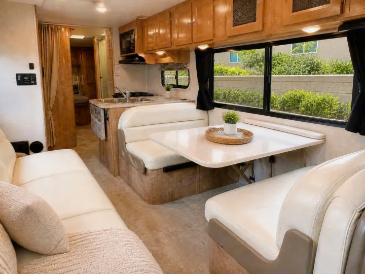 This spacious RV rental interior features a sofa, dining booth, and full kitchen, with light wood cabinets and cream upholstery.. Forest River Coachmen Leprechaun 2020