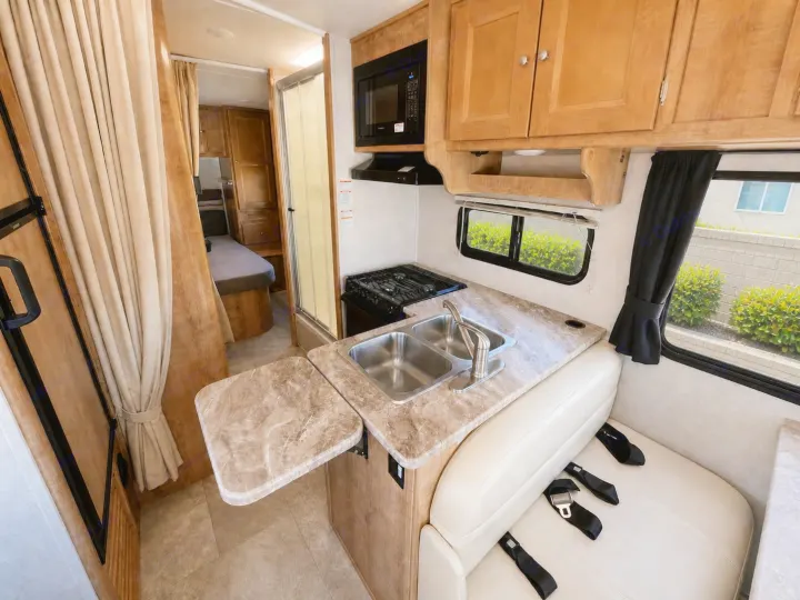 This RV rental offers a compact kitchen with a sink, stovetop, microwave, dining bench, and views of the bedroom and shower.. Forest River Coachmen Leprechaun 2020