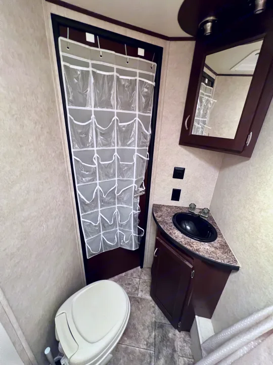RV rental bathroom with toilet, dark sink vanity, and clear over-door shoe organizer for smart storage.. Crossroads Sling Shot 2012