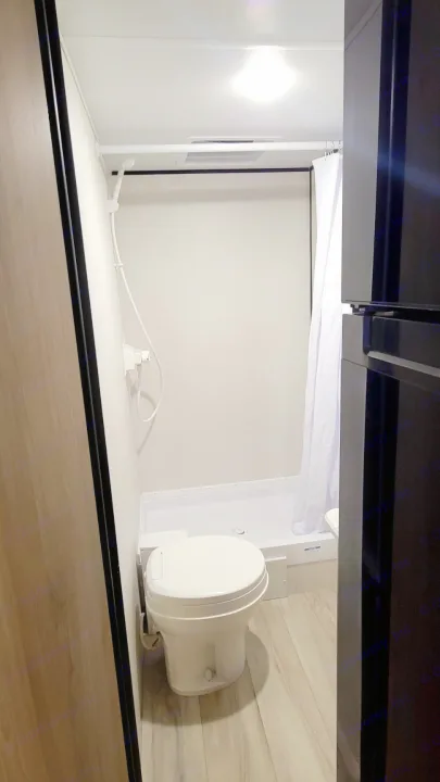 Compact RV rental bathroom with a white toilet, curtained shower, and ceiling vent visible.. Dutchmen Coleman 2025