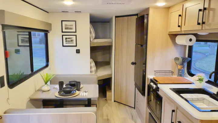 This RV rental interior features a cozy dining area, a well-equipped kitchen with a sink and stove, and comfortable bunk beds.. Dutchmen Coleman 2025