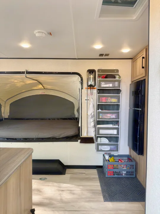 RV rental interior: A compact living space with a pop-out bed, vertical storage organizer, and refrigerator.. Keystone Coleman 13T 2026