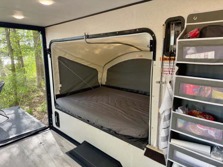 RV rental camper interior featuring a comfortable pop-out bed, scenic forest view, and practical hanging storage.. Keystone Coleman 13T 2026