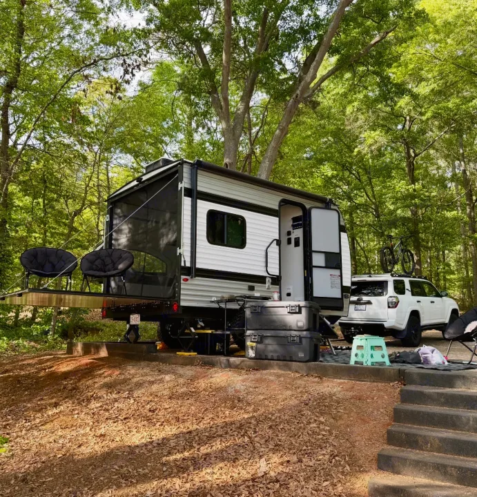 This RV rental, a travel trailer with a rear patio, is perfectly set up at a forested campsite with an SUV and bike.. Keystone Coleman 13T 2026