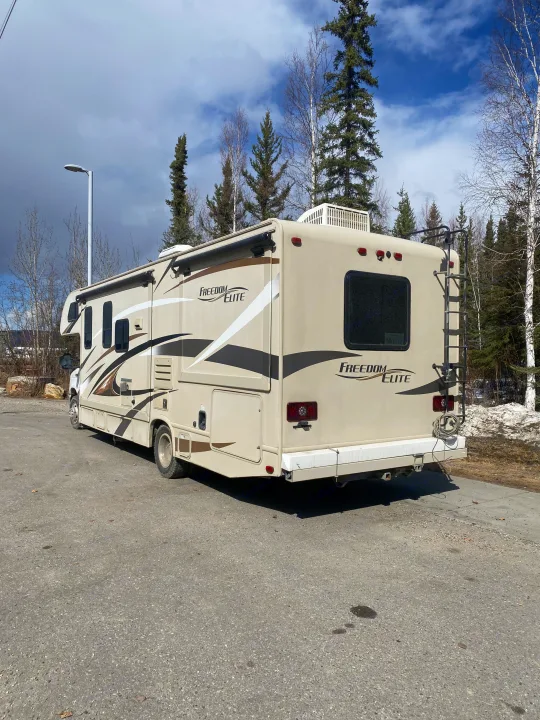 A spacious beige Freedom Elite RV rental is parked on asphalt with trees and melting snow in the background under a cloudy sky.. Thor Freedom Elite 2016