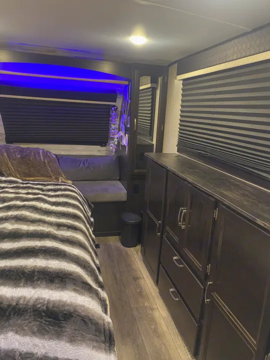 Cozy RV rental bedroom featuring modern dark wood cabinetry, blue ambient lighting, and a plush striped bed for comfort.. Jayco White Hawk 2020