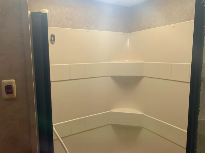Clean RV rental shower stall featuring white paneled walls, built-in corner shelves, and a showerhead holder.. Keystone RV Sprinter 250RBS 2008