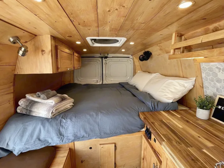 Interior of a cozy wooden camper van rv rental, showcasing a bed, storage, and natural wood finishes.. Gmc Savanna 2500 2016