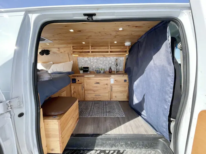 Cozy rv rental van interior with a comfortable bed, wooden kitchenette, and elegant finishes, seen through the open door.. Gmc Savanna 2500 2016