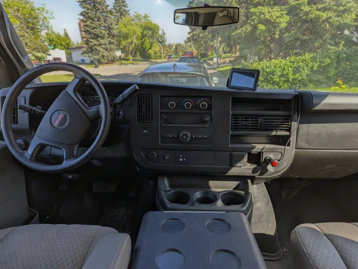 Driver's view inside a GMC commercial van or RV rental, featuring the dashboard, steering wheel, and a sunny street ahead.. Gmc Savanna 2500 EXT 2016