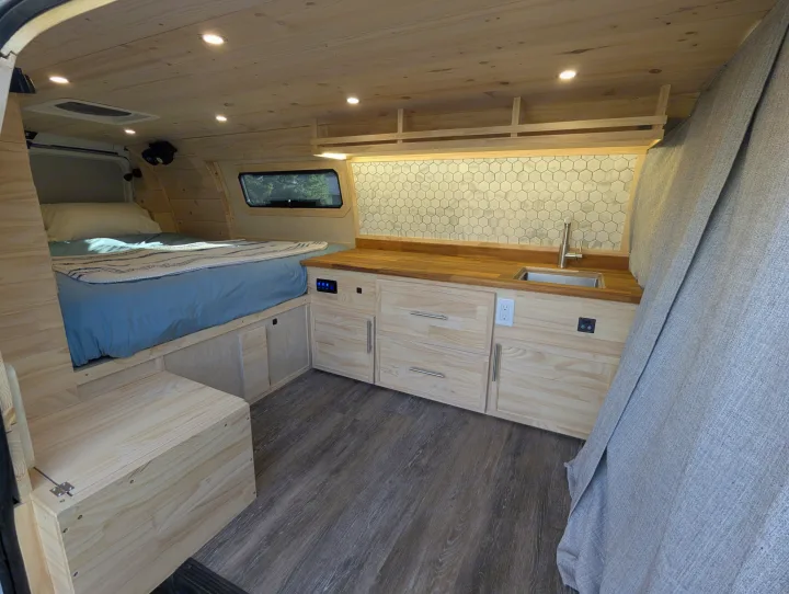 Bright rv rental interior: light wood panels, blue bed, kitchenette with hexagon backsplash, and dark wood floor.. Gmc Savanna 2500 EXT 2016