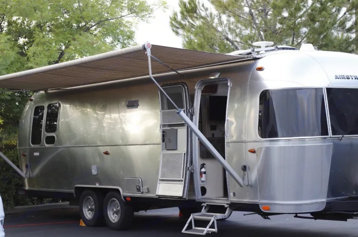 This silver Airstream travel trailer, potentially an RV rental, is set up with its side awning extended and entry door open.. Airstream International 2020