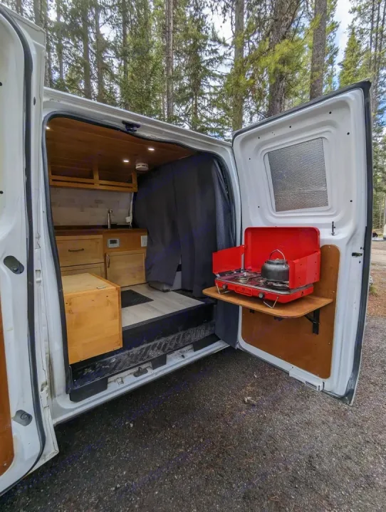 RV rental camper van interior featuring a custom kitchen and portable stove on a fold-out shelf, perfect for forest camping.. Gmc Savanna 2500 2015