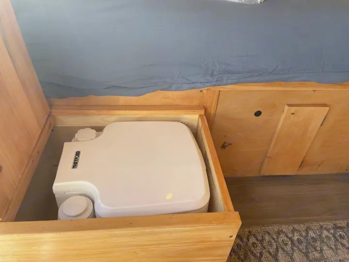 Compact Thetford portable toilet stored under a bed, a practical feature for your next RV rental or campervan adventure.. Gmc Savanna 2500 2015