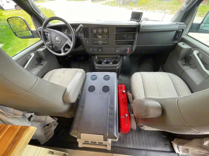 Inside an RV rental van: driver's area with dashboard, steering wheel, and front seats, plus a cooler and red toolbox.. Gmc Savanna 2500 2015