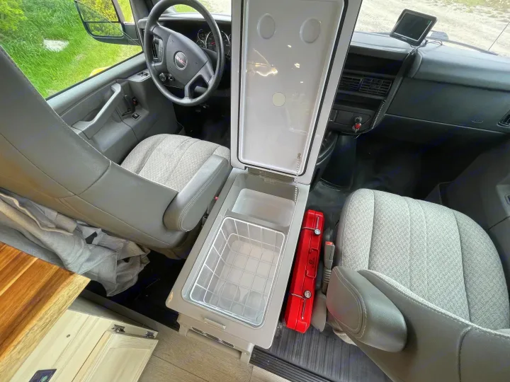 Inside this rv rental's front cabin, an open portable fridge sits between seats, with a red toolbox on the floor.. Gmc Savanna 2500 2015