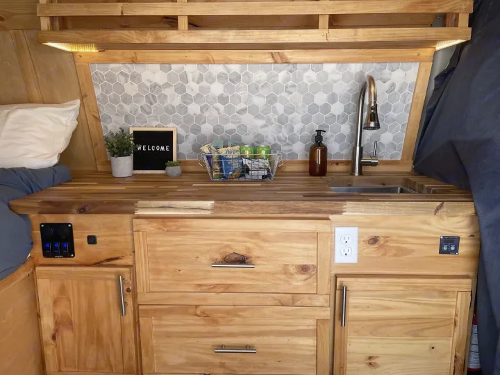 Cozy RV rental interior with custom wood kitchen, sink, storage, and sleeping area. Enjoy practical design for travel.. Gmc Savanna 2500 2016