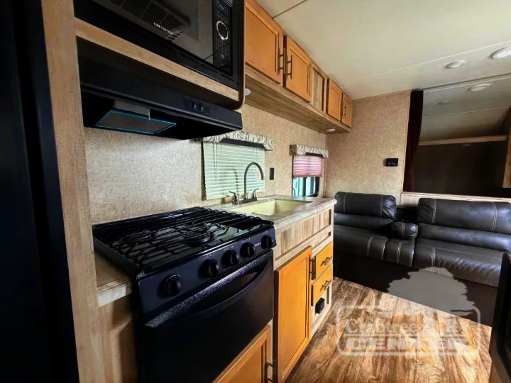 Inside this RV rental: a modern kitchen with black appliances, light wood cabinets, and dark leather-look sofa seating.. Coachmen Other 2020