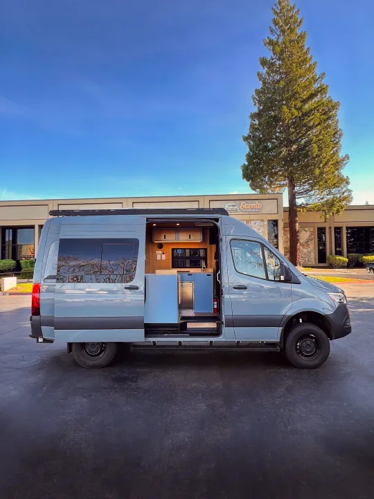 Light blue camper van (RV rental) with its side door open, revealing a modern custom interior. Parked at Scenic RV Rentals.. Mercedes-Benz Sprinter 2024