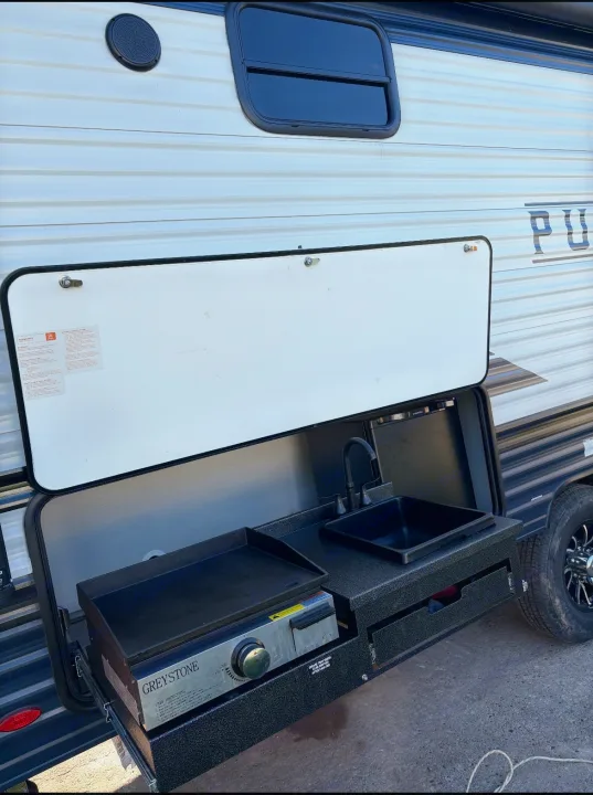 This RV rental travel trailer features an outdoor kitchen with a griddle and sink, ready for campsite cooking.. Puma Palomino 2024
