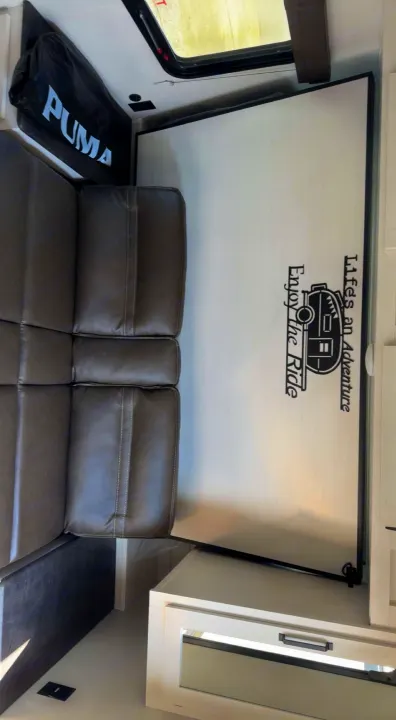 RV rental living area with comfy leatherette sofa, fold-down table featuring an adventure decal, & window view.. Puma Palomino 2024